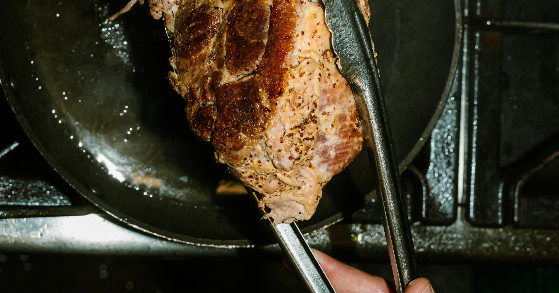 Une pièce de viande saisie, tenue à la pince, en cuisine chez Traiteur Maxime